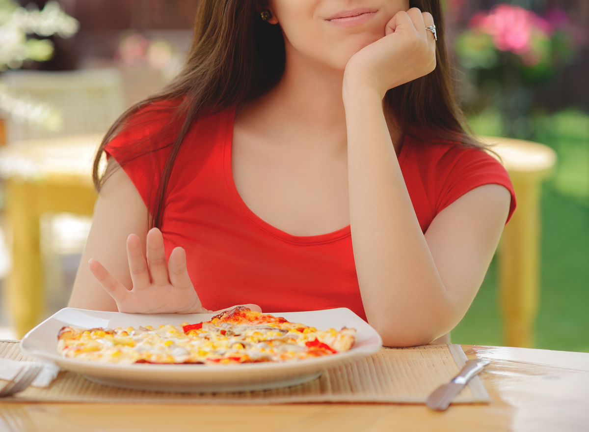 Woman pushing plate of pizza away to skip a meal