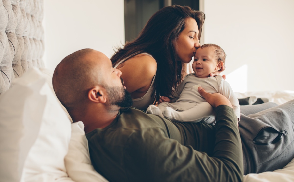 A couple with their first baby giving a kiss.