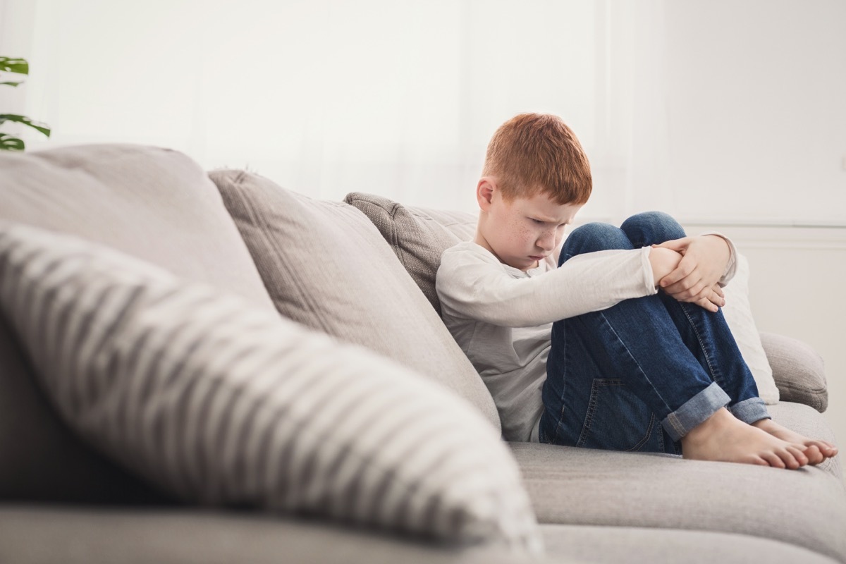 upset kid sitting on couch with his arms around his legs