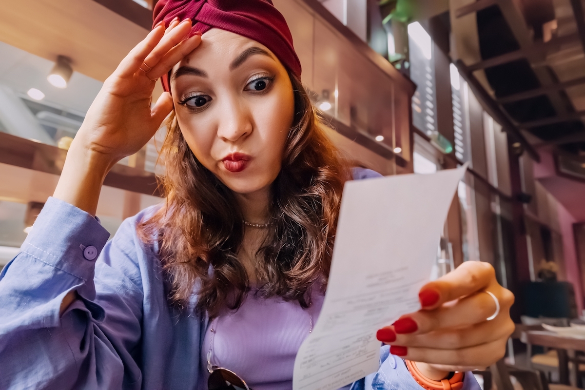 Closeup of a young woman in a restaurant looking unhappily at the bill