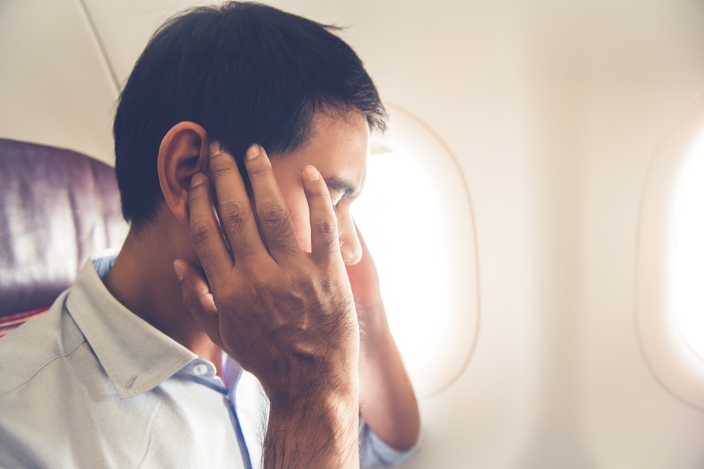 Man on an airplane holding his ears in pain.