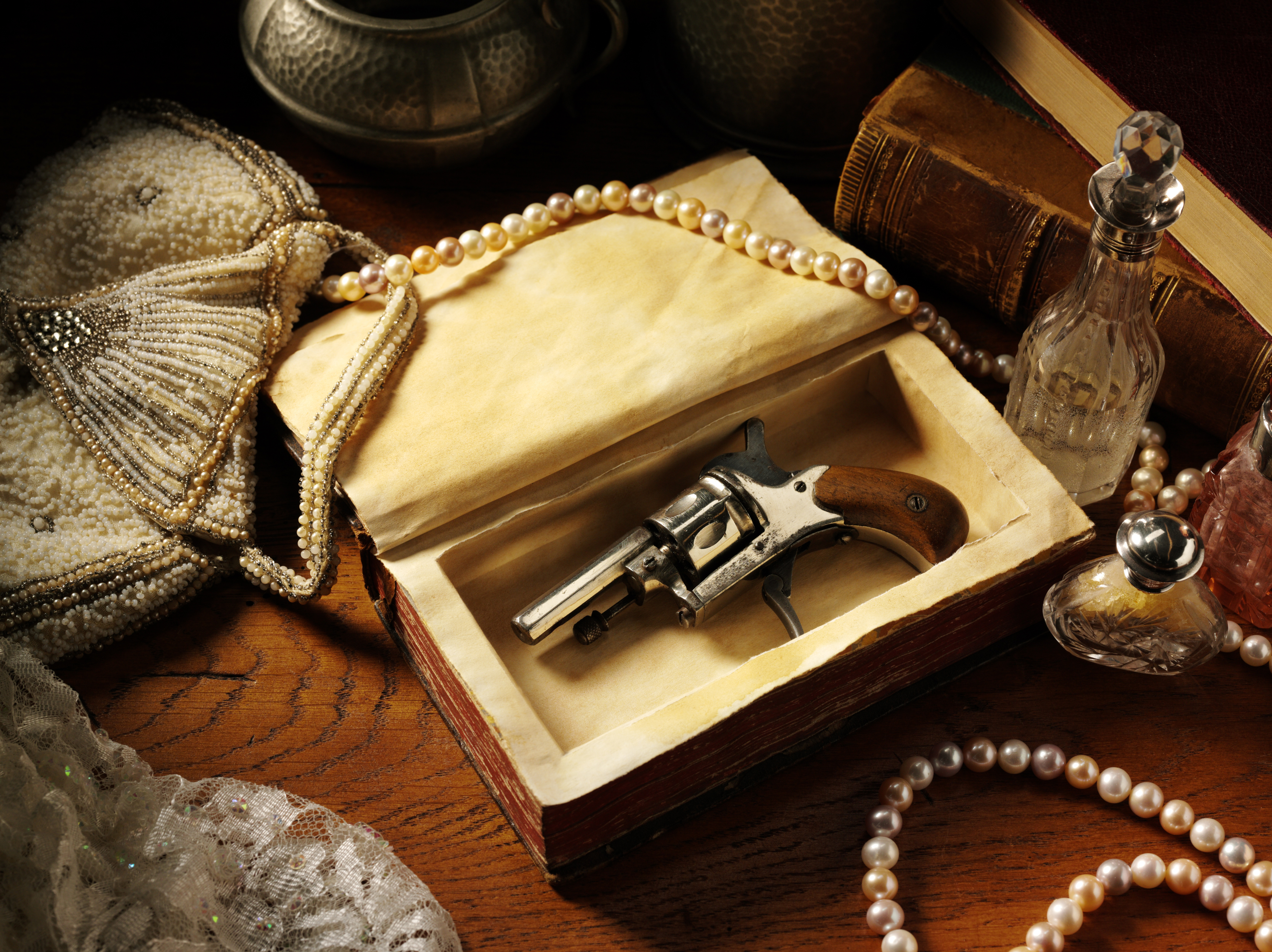 Vintage themed image of a Edwardian gun, snuff bottle and pearls on a old wooden table.