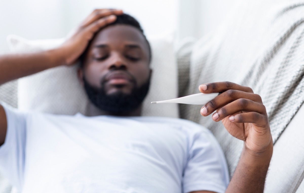 black man on couch looking at thermometer