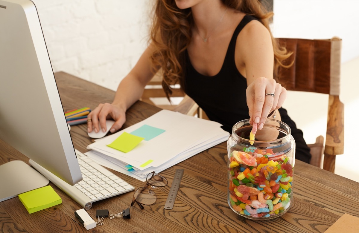 Young woman eating sweets at workplace in office.