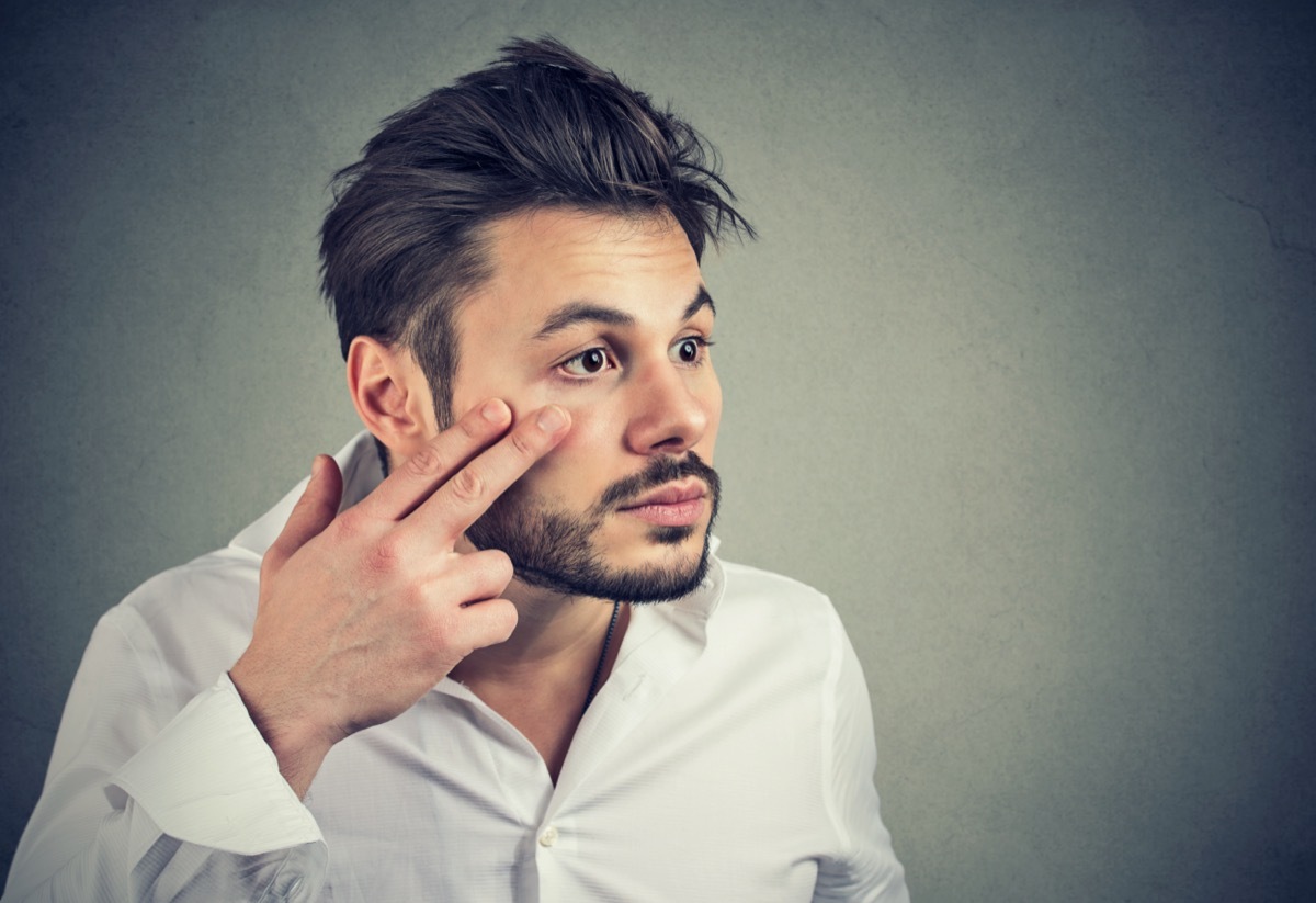 man pulling down eyelid checking his eye looking in mirrow feels unwell has black circles