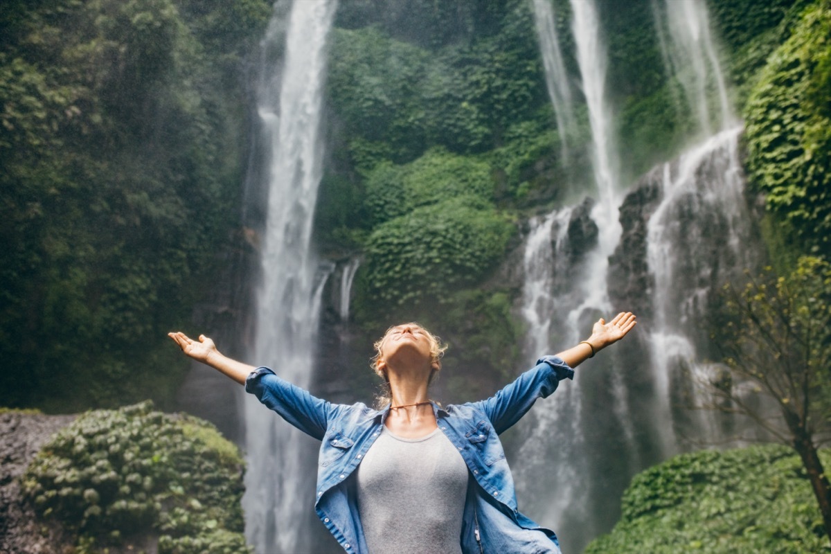 Woman With Arms Wide Open under a Waterfall