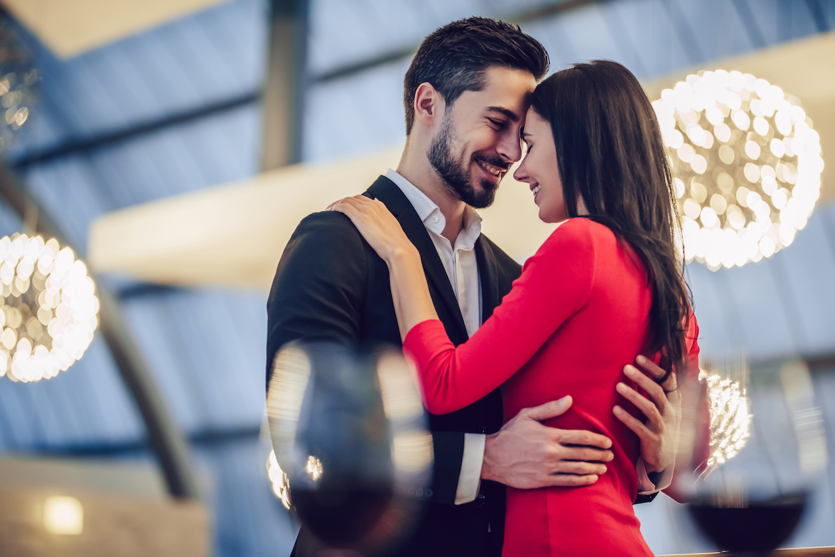 Man and woman hugging at a restaurants. She's wearing a red dress.