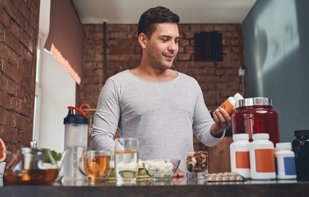 30-something man with brown hair holding supplements in front of a counter covered in bottles