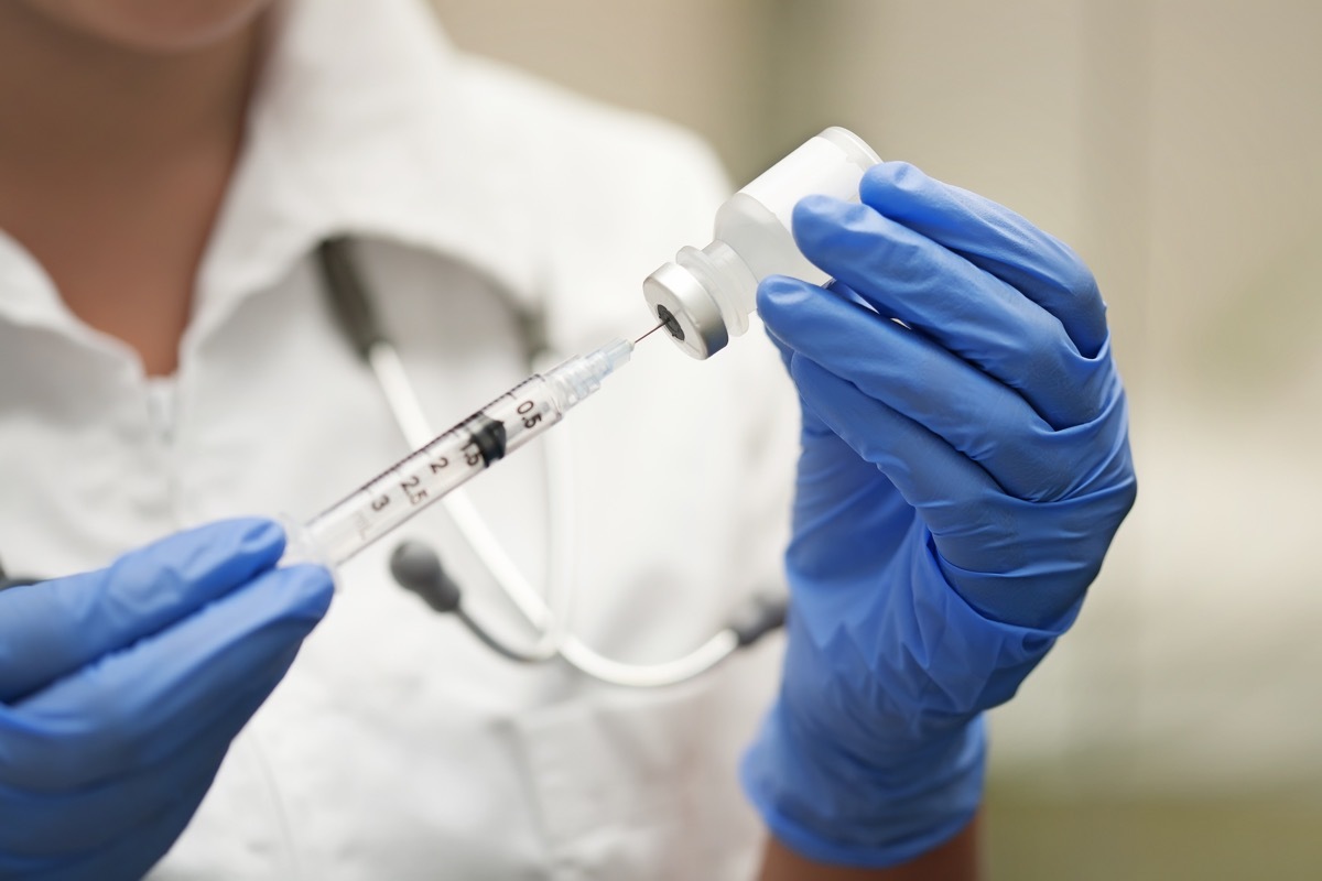 Medication nurse wearing protective gloves and white scrubs get a needle or shot ready for an injection. - Image