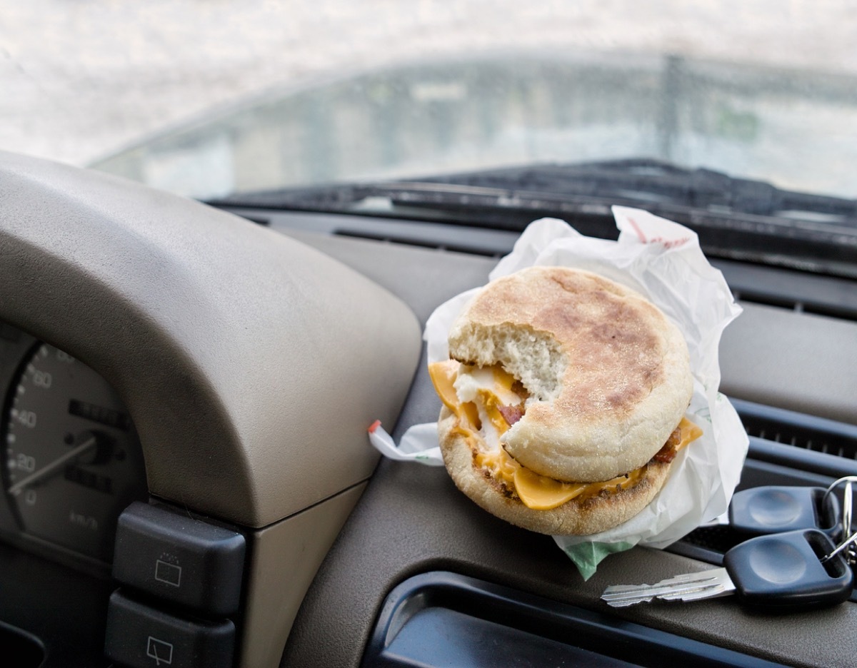 A bitten sandwich next to the ignition keys laid on a car dashboard, concept of having a coffee break while travel by car