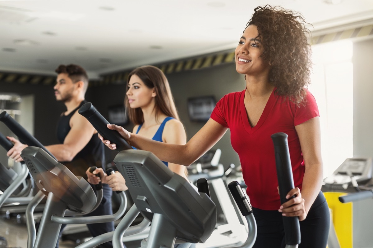 young black woman exercising on the elliptical at the gym with two other young people in the background