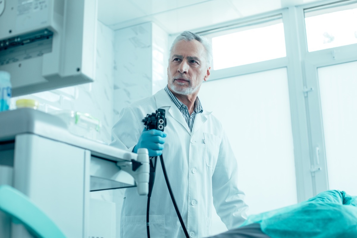 Calm mature medical worker standing with an endoscope and looking at the screen stock photo