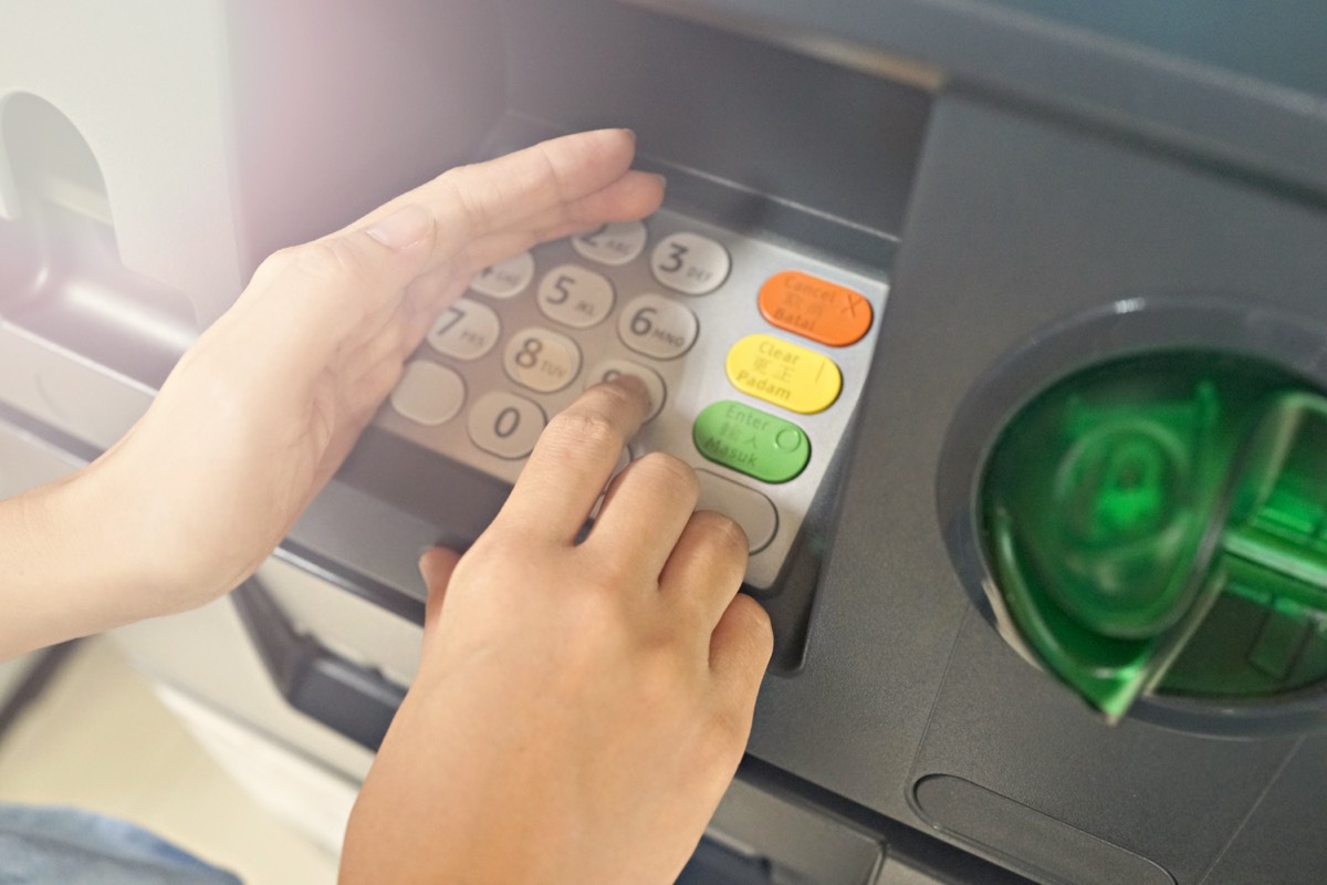 Close up of female hand entering PIN/pass code on ATM/bank machine keypad, she hides it with other hand for security purposes