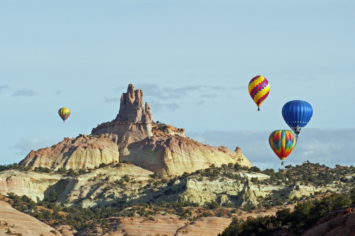 A group of hot air balloons rise above the red sandstone of Red Rocks State Park near Gallup, New Mexico, and circle around the Church Rock formation