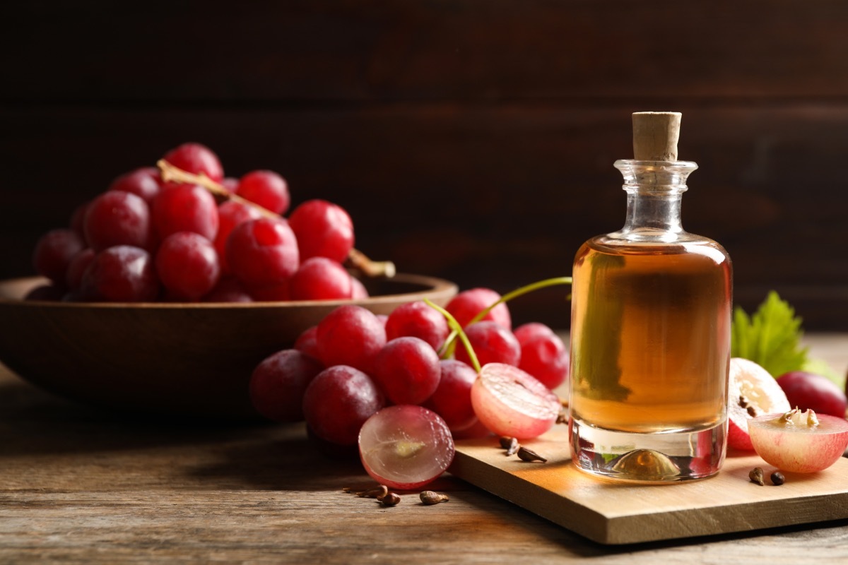 Bottle of natural grape seed oil on wooden table, space with text. Organic cosmetic