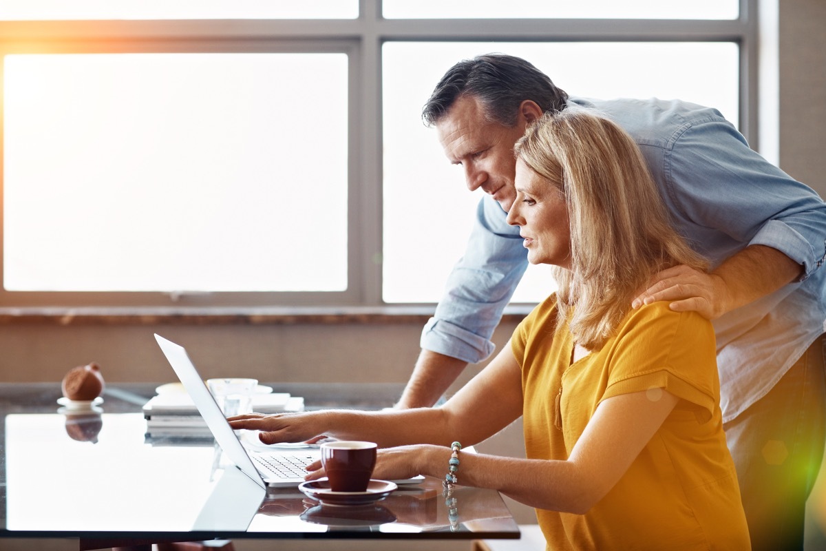 Couple sitting at their dining room table doing online banking using a laptop